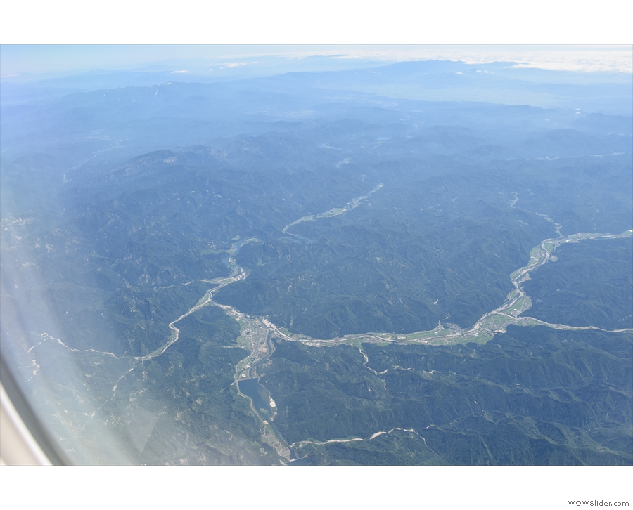 We're flying over a landscape of forested mountains and twisting valleys, with both...