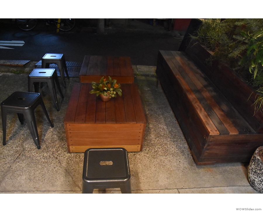 There are a couple of wooden boxes / coffee tables lining a long, wooden bench.