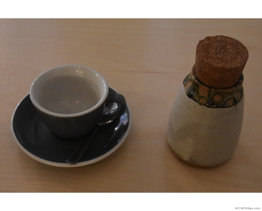 The presentation is excellent, with the coffee in a ceramic flask, cup on one side.