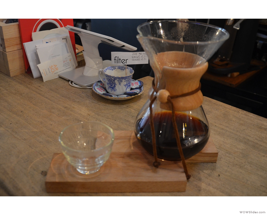 The coffee is served in the Chemex, on a wooden tray, glass on the side.