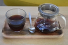 ... served in a carafe on a small wooden tray, with a glass on the side.