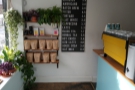 The left-hand wall at the far end of the counter houses the menu and the retail shelves.