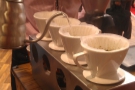 After rinsing the filters, which washes out the paper taste and also serves to warm the cups, the coffee is added and a little water poured into each to allow the grounds to bloom.