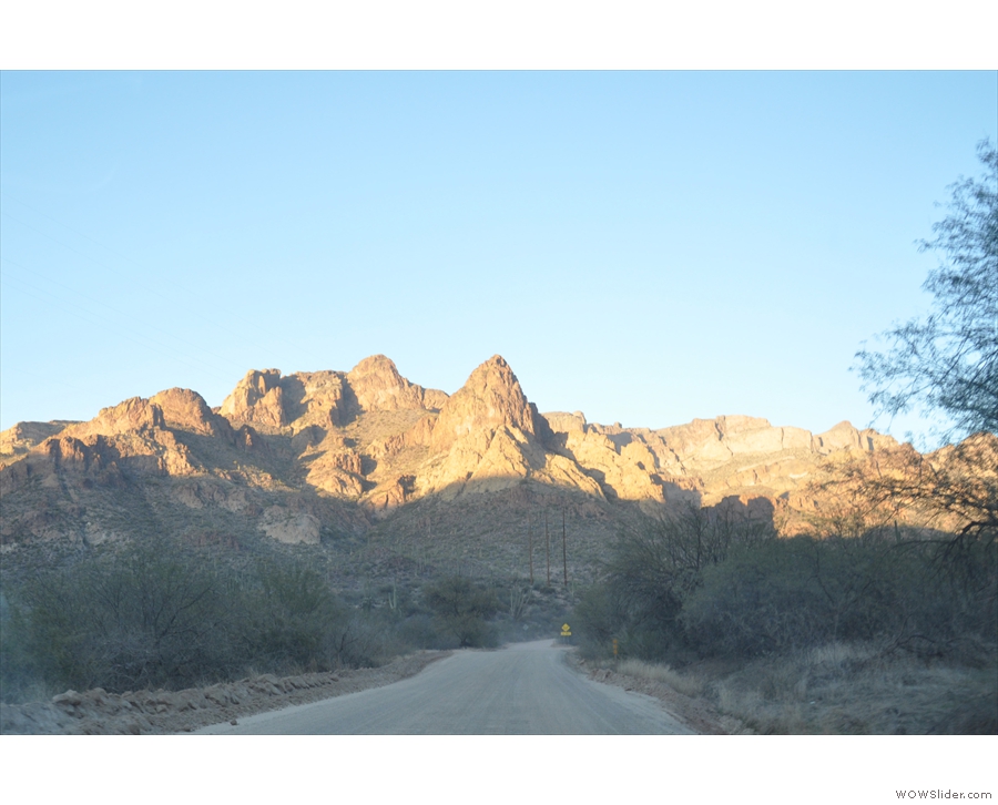 Driving east through a valley on the Apache Trail, the sun setting behind me. The road...