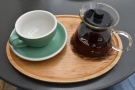 My coffee, served in the carafe, with a cup on the side, all presented on a wooden tray.