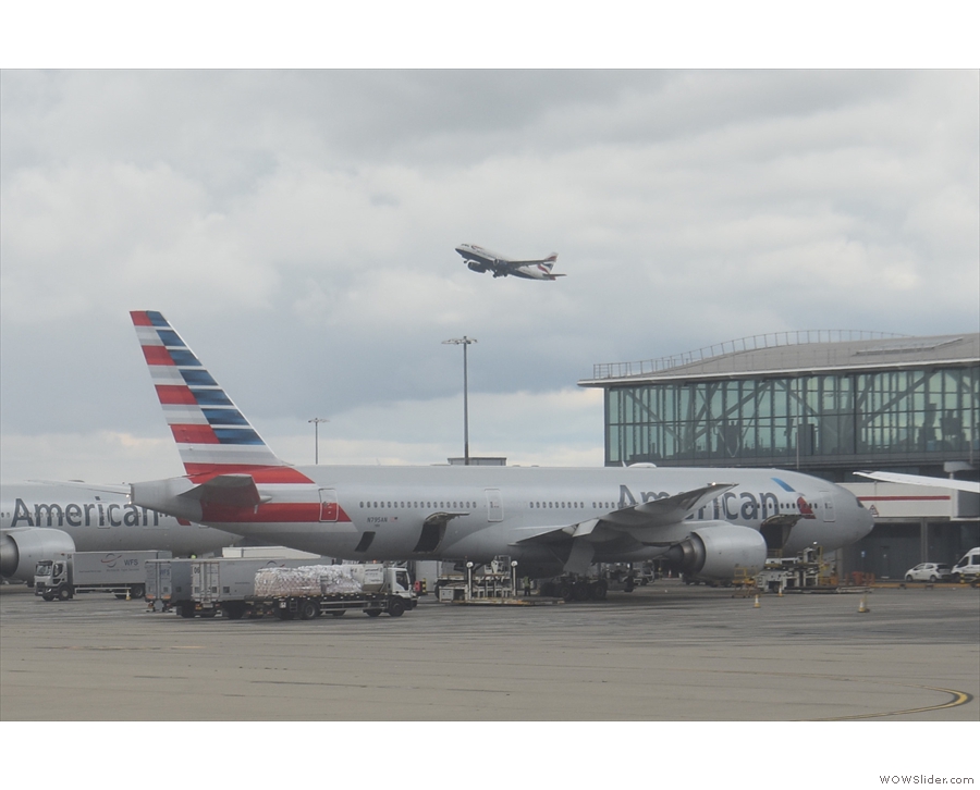 A British Airways A319 takes off over an American Airlines 777-200 waiting to go to JFK.