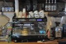The espresso machine is behind the counter, business end facing the customers.