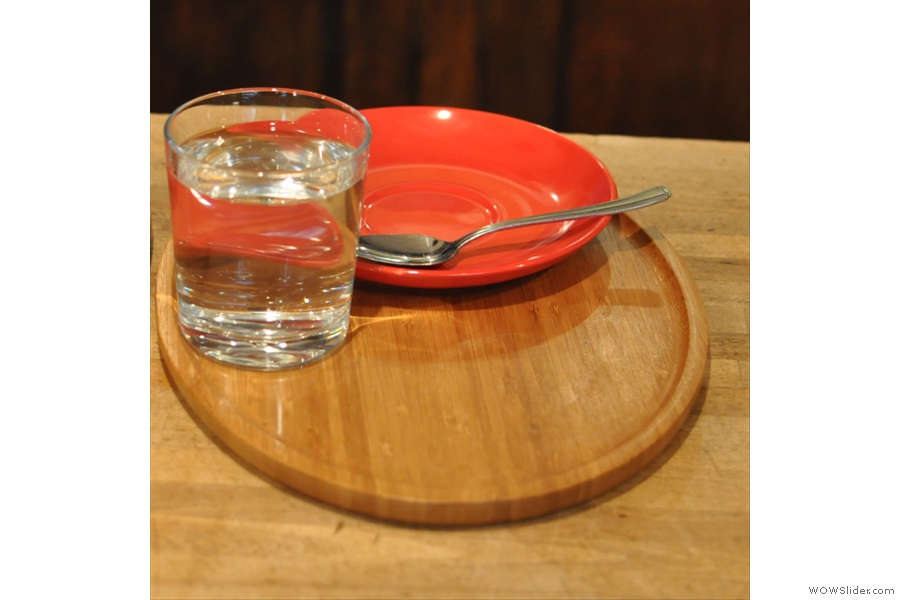 A saucer and its glass of water wait on the tray for the coffee