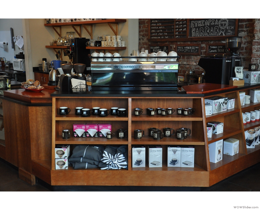 There are retail shelves in the front of the counter, selling merchandising and coffee-kit.